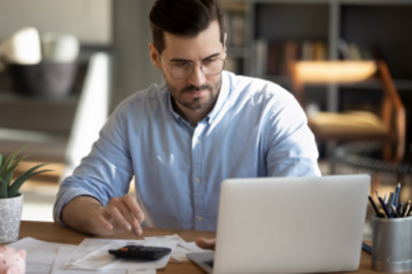 A man sitting at a desk with a laptop and a calculator, working diligently on financial calculations.