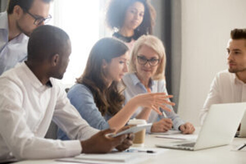 A diverse group of individuals gathered around a table, engrossed in their work on a laptop.