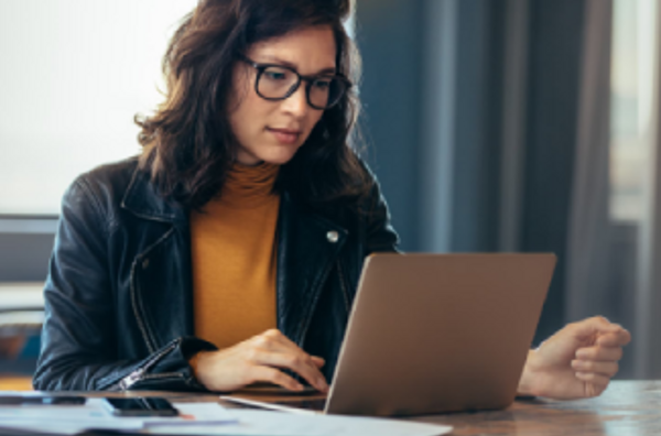 A woman wearing glasses is focused on her laptop, diligently working on her tasks.