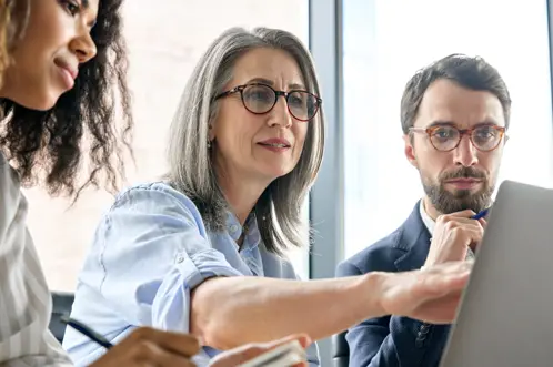 Three professionals gathered around a laptop, intently collaborating and pointing at the screen with serious expressions on their faces