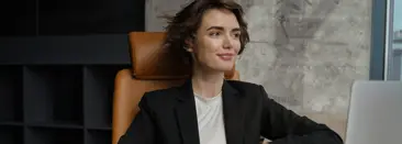 Une femme assise avec un ordinateur portable devant elle, souriante en regardant par la fentre