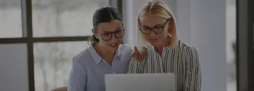 due donne professioniste con gli occhiali, sorridenti mentre guardano lo schermo di un laptop