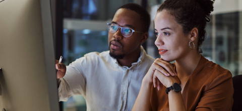 Um homem e uma mulher sentados em uma mesa, ambos com express?es srias enquanto se concentram em uma tela de computador na frente deles