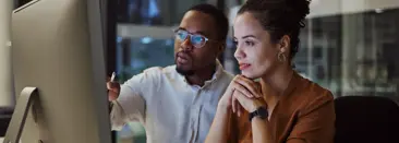 Un uomo e una donna seduti a una scrivania, entrambi con espressioni serie mentre si concentrano sullo schermo di un computer di fronte a loro