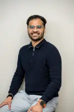 Un uomo che indossa gli occhiali, seduto e sorridente ampiamente, mostrando i denti