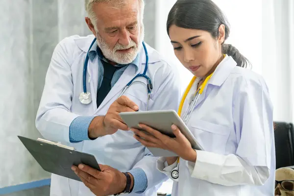 Dois mdicos est?o segurando iPads; O mdico ajuda a mdica apontando para algo em sua tela
