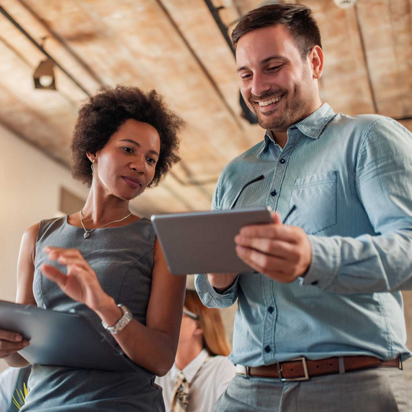 A woman and a man stand together, smiling as they look at an iPad screen