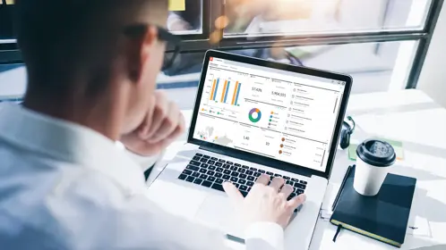 Business man analyzing financial charts on laptop with coffee on desk
