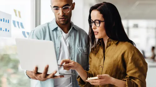 Man standing and showing laptop to woman who is pointing at the laptop screen