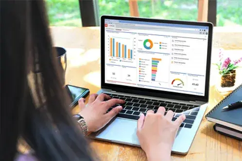 Eine Frau sitzt an einem Schreibtisch, tippt auf einem Laptop und analysiert ein Dashboard