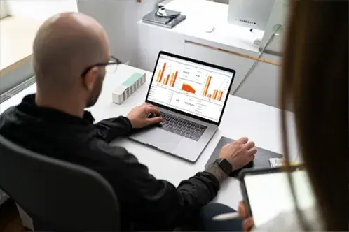 Un homme assis  un bureau, tapant sur son ordinateur portable et analysant un tableau de bord