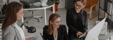Three people in a work setting discussing reports and looking at their computer screen