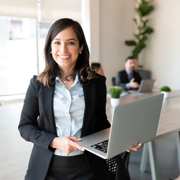 A professional woman stands smiling while holding a laptop