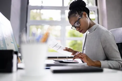 A woman wearing glasses is focused on her computer screen, diligently working on her tasks