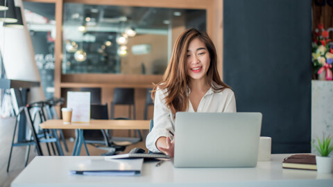 An Asian woman focused on her laptop, working diligently in a cozy café setting.