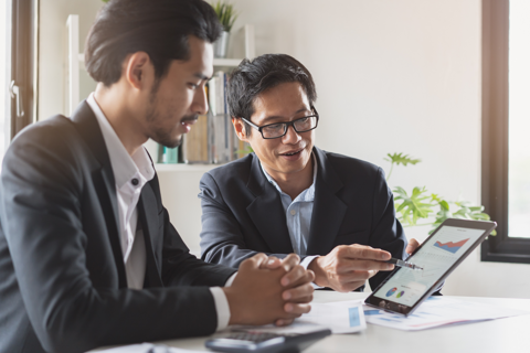 Two businessmen focused on a tablet computer, discussing business matters.