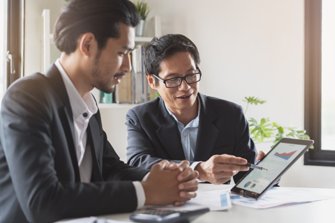 Two businessmen focused on a tablet computer, discussing business matters.
