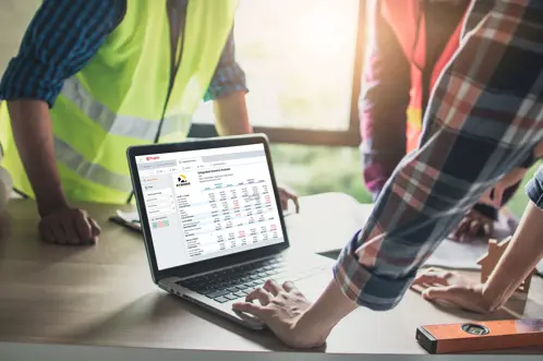 Een team dat bouwvesten draagt, staat samen en werkt samen terwijl ze financile gegevens bekijken die op een laptopscherm worden weergegeven