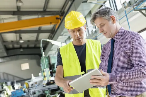 Twee mannen met veiligheidshelmen die een tablet onderzoeken, mogelijk bouwplannen bespreken of een bouwplaats inspecteren