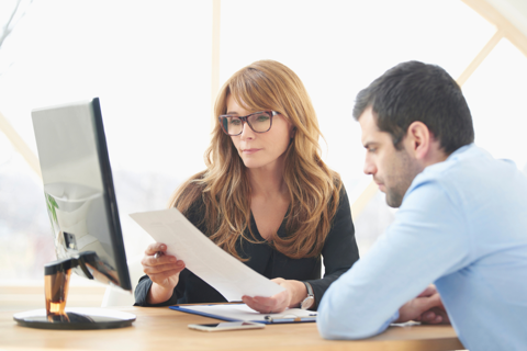 A man and woman sitting at a desk, reviewing paperwork together.