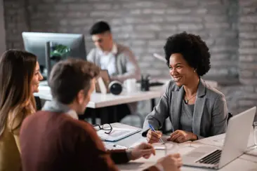 Een diverse groep mensen zit rond een tafel, verdiept in hun werk op laptops