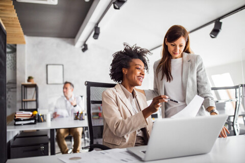 Two businesswomen collaborating on a laptop in a professional office setting.