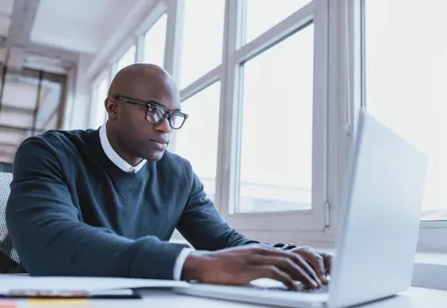 Een man met een bril is gefocust op zijn laptop, verdiept in zijn werk