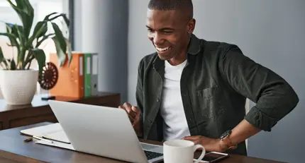 Un uomo seduto alla sua scrivania e sorridente al suo laptop