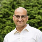 A man in a white shirt and glasses, smiling while standing outdoors