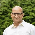 A man in a white shirt and glasses, smiling while standing outdoors