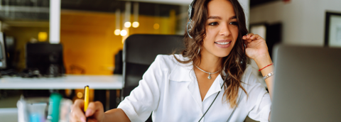 Een vrouw in een wit overhemd zittend aan een bureau, werkend aan een laptop
