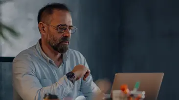 Ein Berufsttiger mit Brille sitzt da und schaut mit ernster Miene auf seinen Laptop-Bildschirm