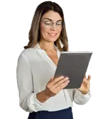 Una mujer con una blusa blanca, con gafas, de pie y sonriendo a la pantalla mientras sostiene un iPad