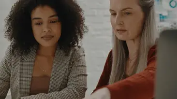 Zwei Frauen, die gemeinsam Dokumente begutachten und sich in eine ernsthafte berufliche Diskussion vertiefen