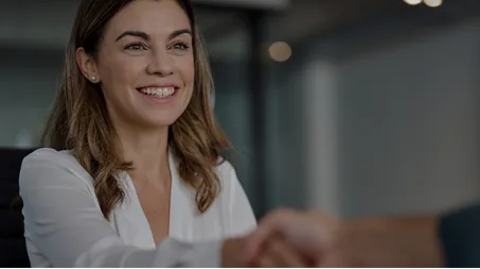 A woman in a white shirt smiles as she shakes hands with someone