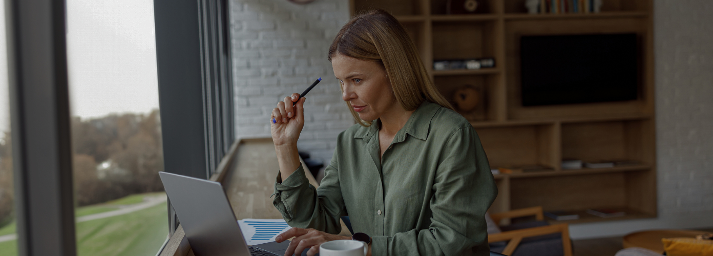 Eine Geschftsfrau, die in einem gemtlichen Bro an einem Laptop arbeitet, whrend sie in der Nhe von Fenstern sitzt
