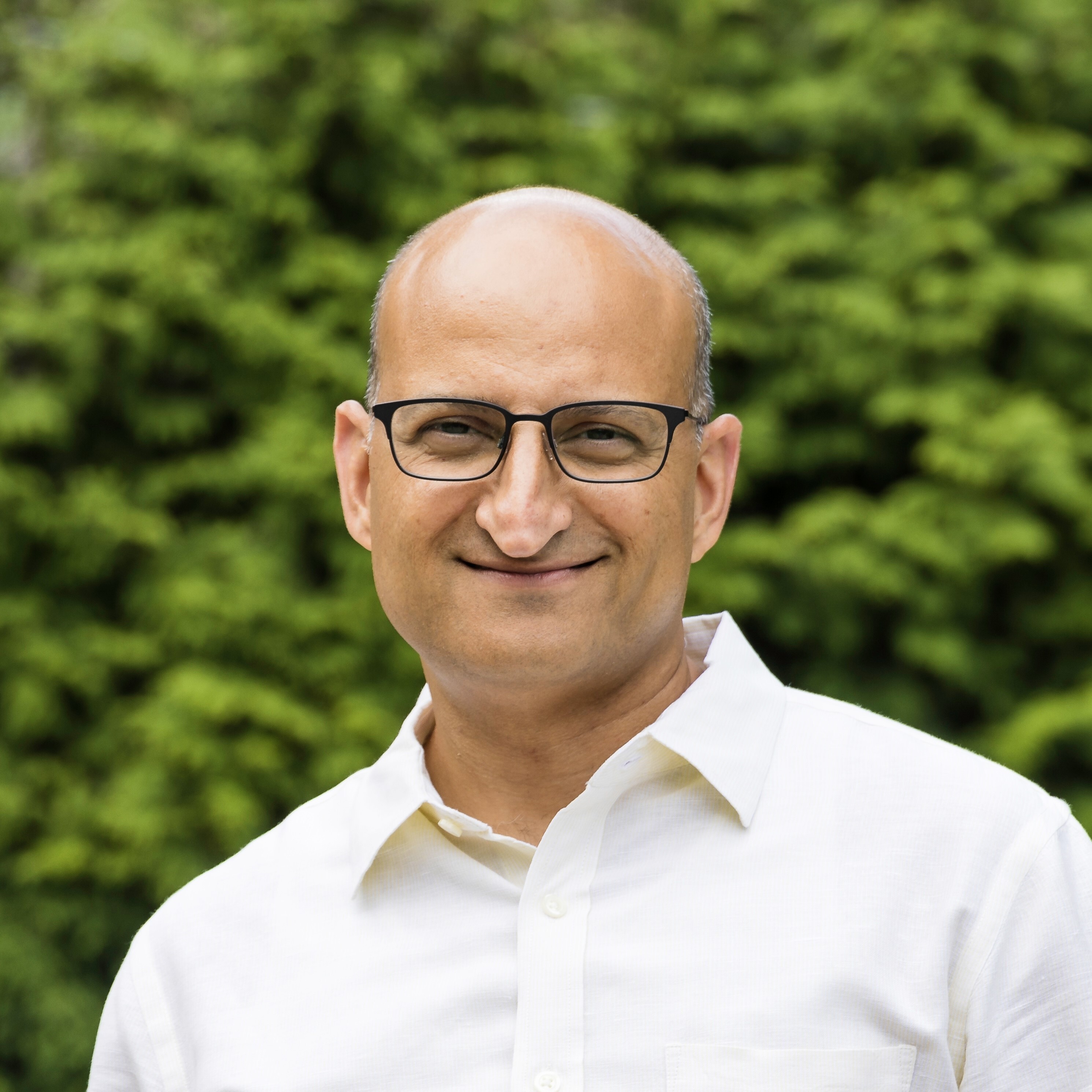 A man in a white shirt and glasses, smiling while standing outdoors