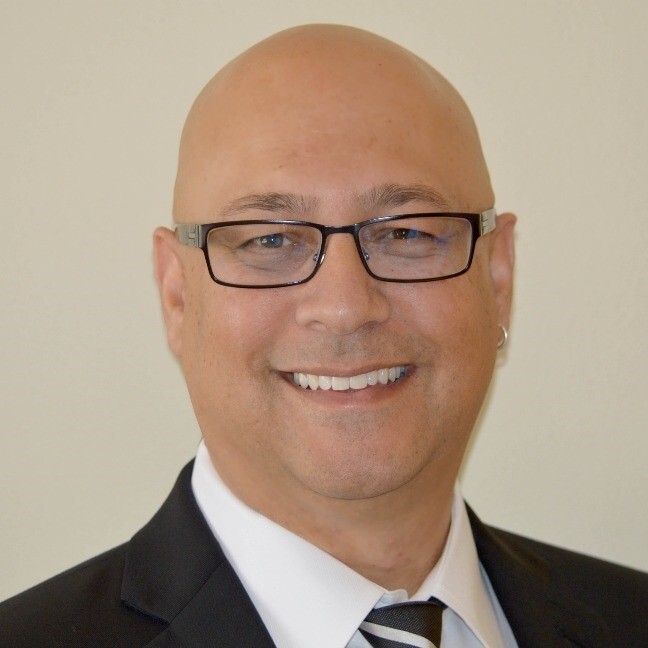 A close-up of a man in a suit and glasses, standing and smiling