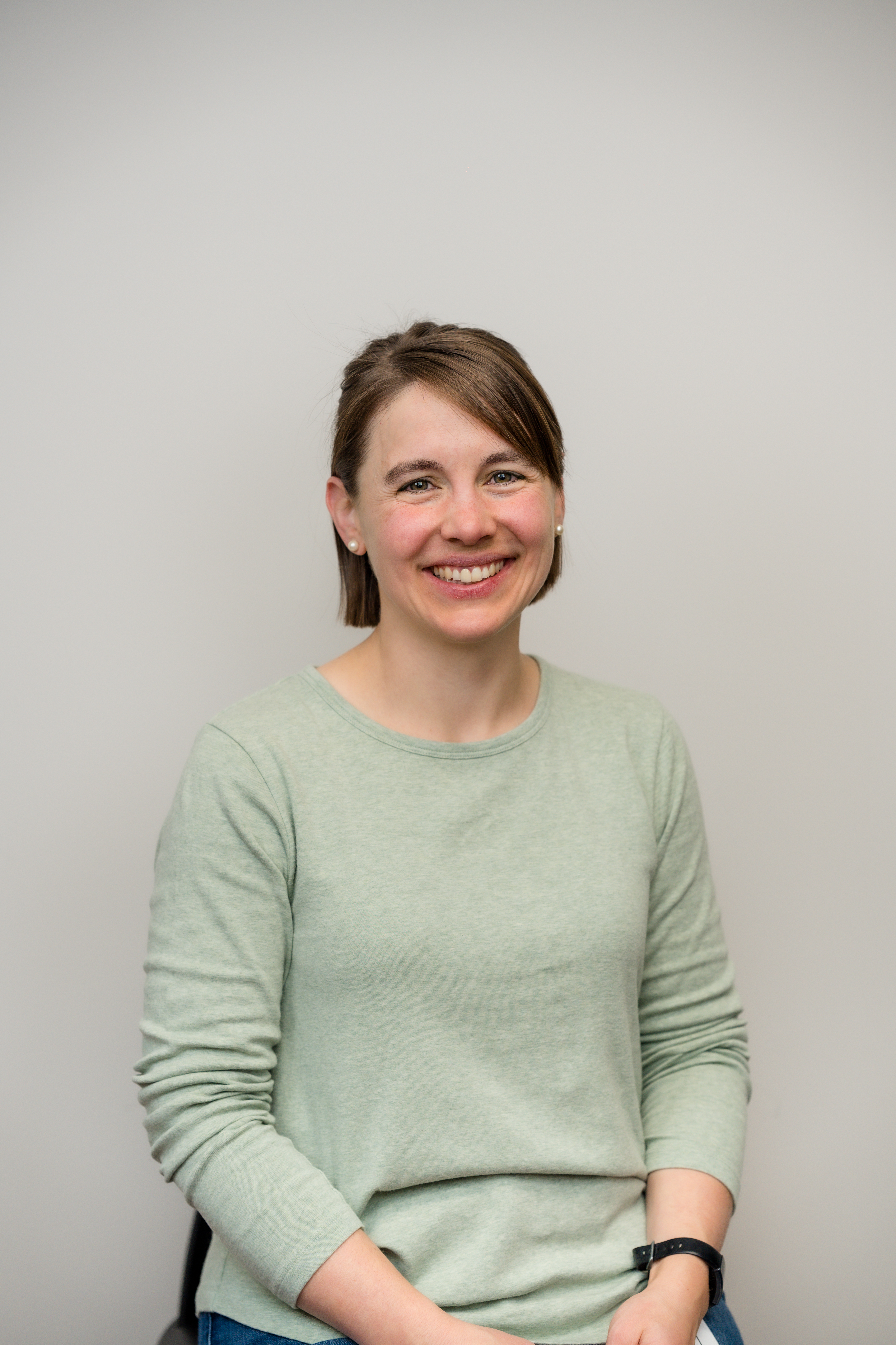 A woman in a light green shirt, seated and smiling warmly