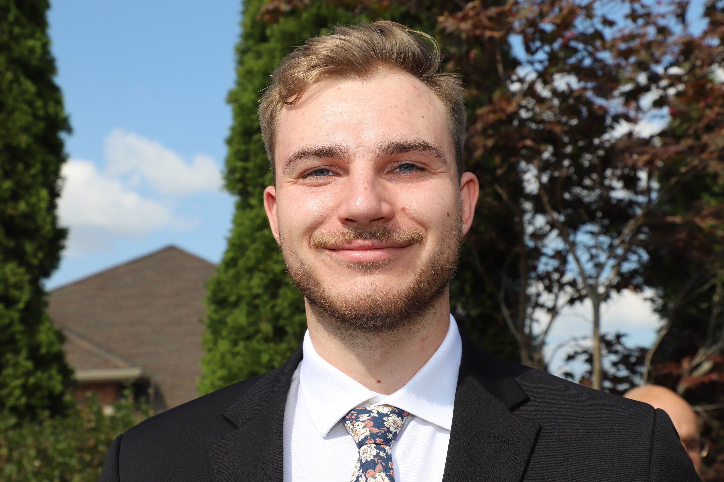 A man wearing a suit smiling and standing outside
