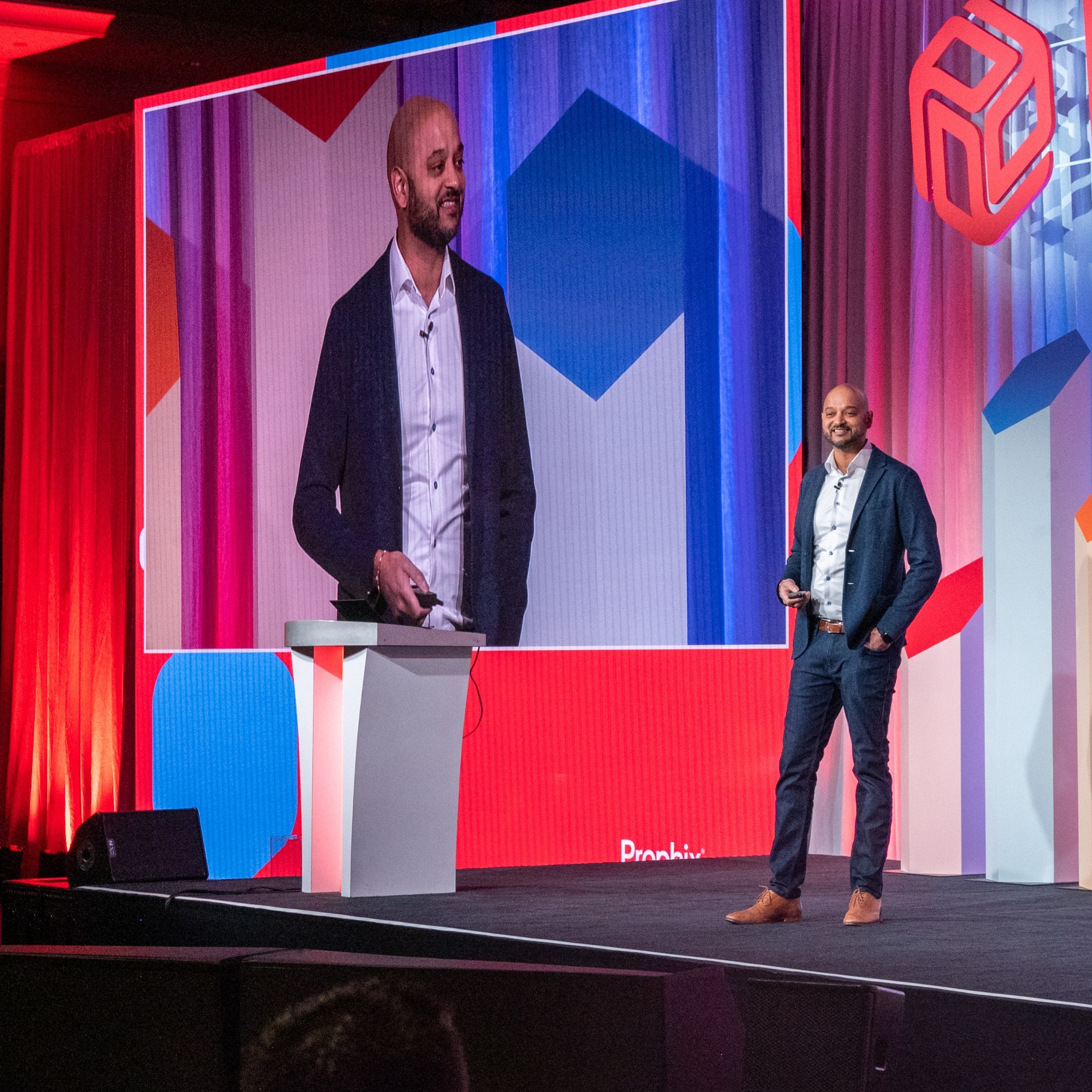 Speaker on stage at conference with live broadcast on projector screen