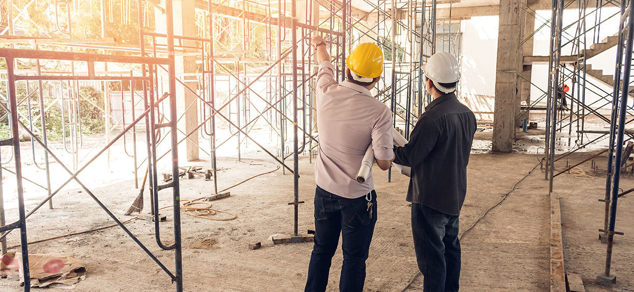 Two men in hard hats standing in front of scaffolding, working on a construction site.
