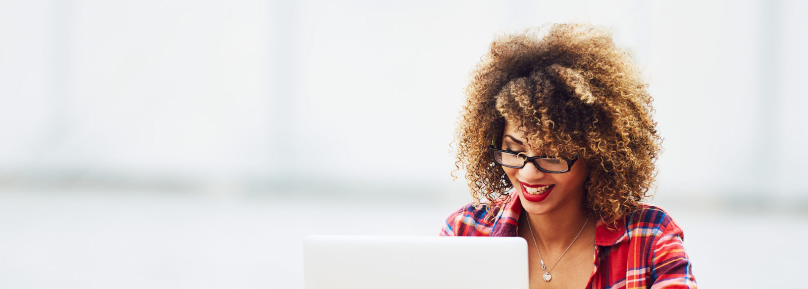 A woman wearing glasses smiling at her laptop