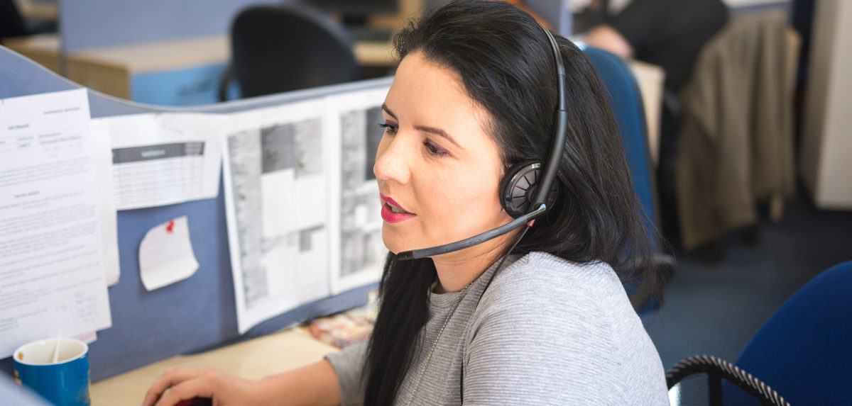 Una mujer que lleva un auricular, trabajando en un entorno de oficina, asistiendo a clientes o participando en actividades de telecomunicaciones.