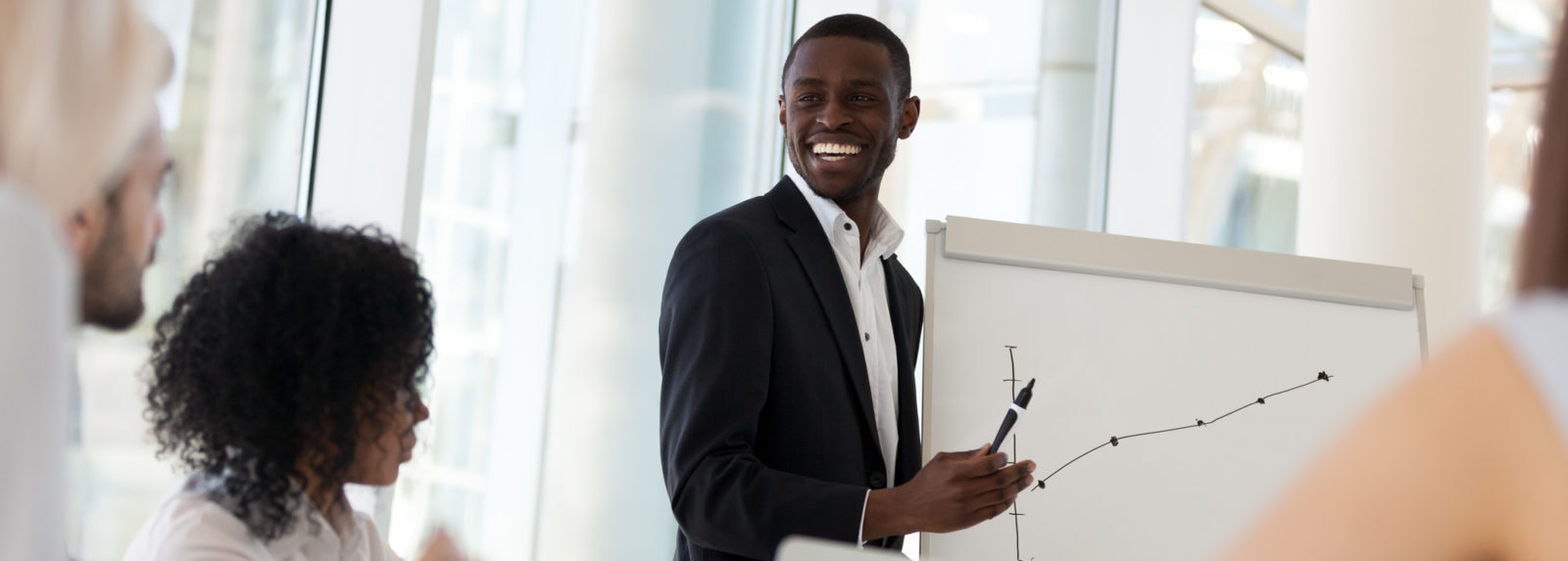 A professional man in a suit presenting to his colleagues in a meeting room