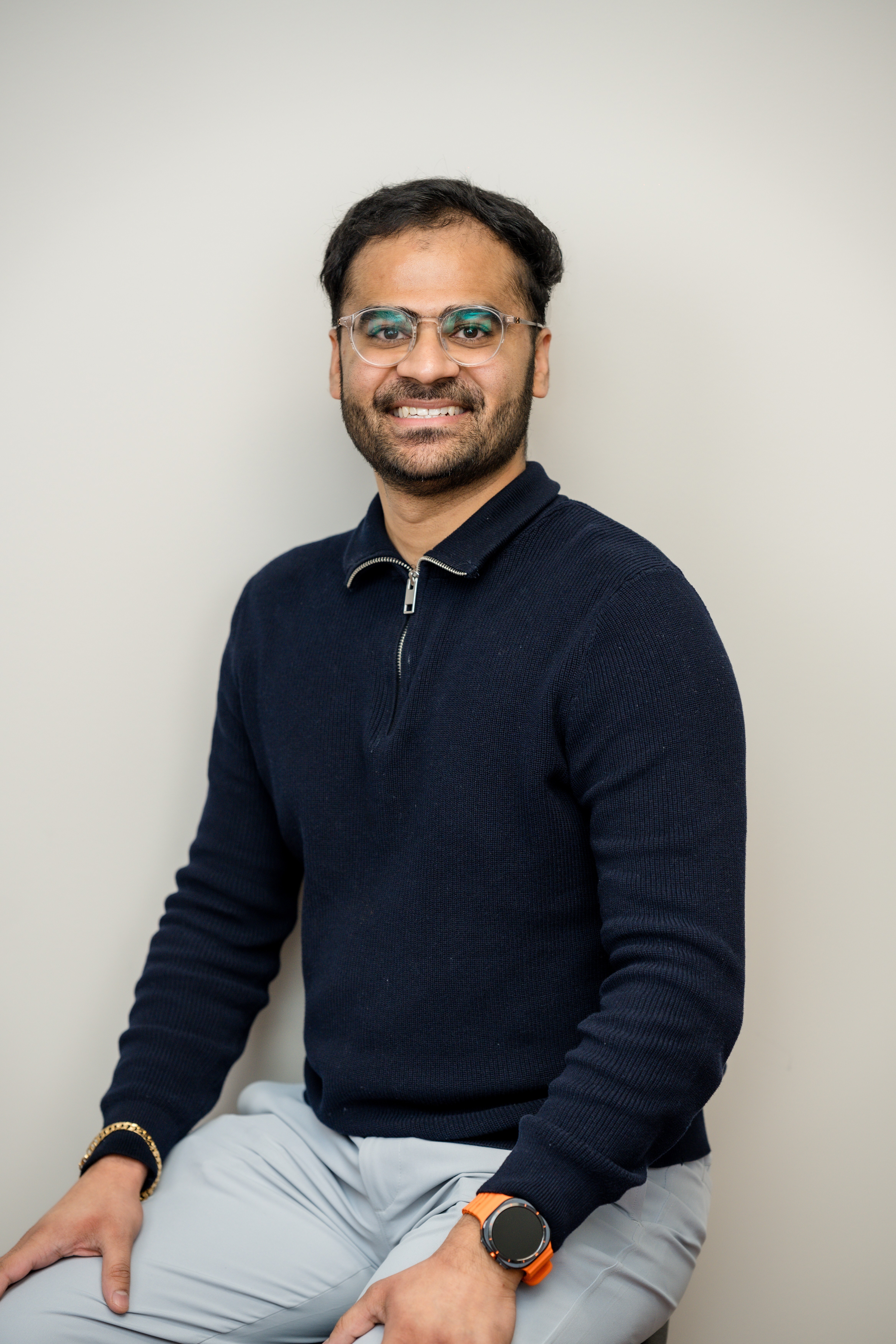 A man wearing glasses, seated and smiling broadly, showing his teeth