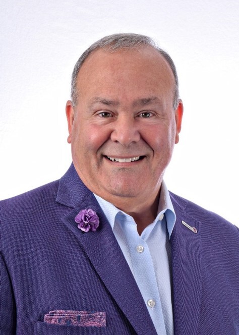 Tom Hood A man in a purple suit and tie, wearing a smile on his face.