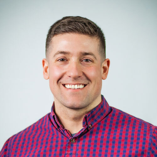 A man wearing a purple and pink dress shirt smiling