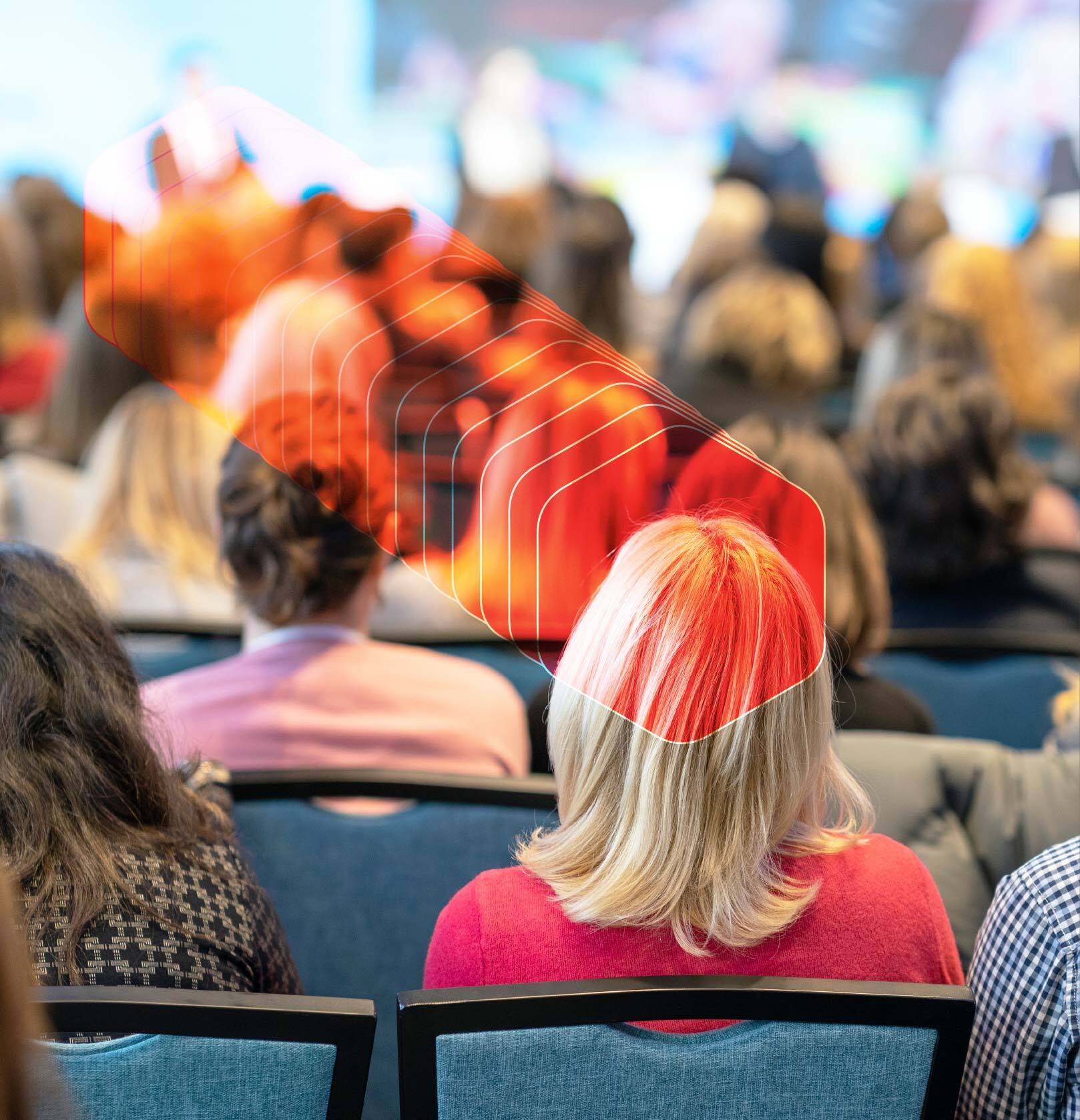 A large audience seated, facing away, with their attention directed toward a stage