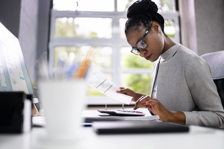 Eine Frau mit Brille ist auf ihren Computerbildschirm fokussiert und arbeitet fleig an ihren Aufgaben
